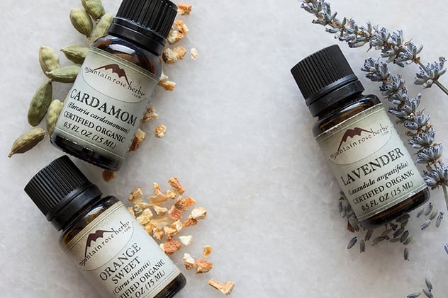 Lavender, orange, and cardamom essential oils laying on counter with their botanicals